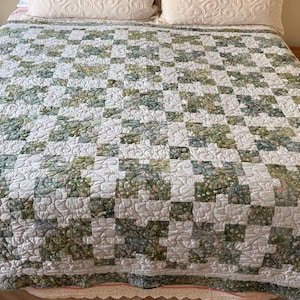 May include: A quilted bedspread with a white background and a repeating pattern of green and white squares. The bedspread is on a bed with white pillows and wooden nightstands on either side.