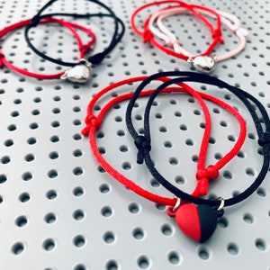May include: Two sets of friendship bracelets with heart charms. One set is red and black, the other is pink and red.