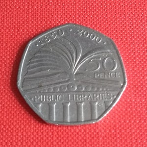 Puede incluir: Una moneda de 50 peniques de plata que conmemora el 2000 aniversario de las bibliotecas públicas en el Reino Unido. La moneda presenta un libro abierto con un árbol que crece de él, y el texto "1850 - 2000 PUBLIC LIBRARIES 50 PENCE".