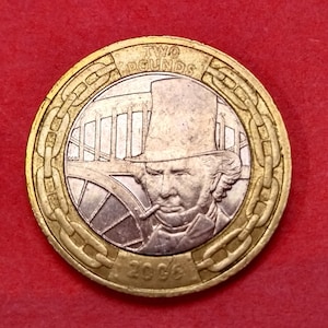 May include: A gold-colored two pound coin featuring a portrait of Isambard Kingdom Brunel, a British engineer, and the words "TWO POUNDS" and "2006".