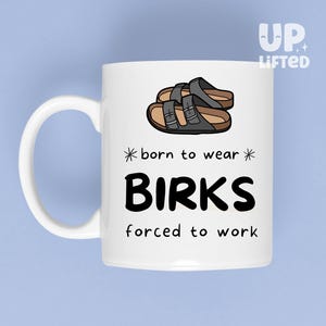Peut inclure: Mug en c&eacute;ramique blanche avec une anse, orn&eacute; d'une illustration de sandales Birkenstock noires et marron. Le texte dit "born to wear BIRKS forced to work". Le mug porte le logo "Up Lifted".