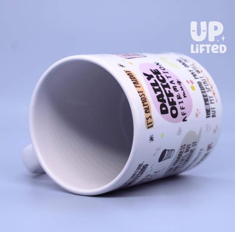Pu&ograve; includere: Tazza in ceramica bianca con la scritta "DAILY OFFICE AFFIRMATION mug" in un ovale rosa. La tazza ha anche la scritta "IT'S ALMOST FRIDAY" e altre frasi. La tazza ha un manico bianco ed &egrave; inclinata.