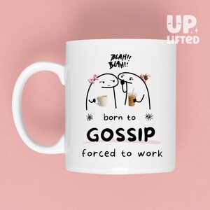 May include: A white ceramic mug featuring a black line drawing of two stick figures with pink hair accessories, each holding a beverage. Above them is the text BLAH!! BLAH!! and below them is the text born to GOSSIP forced to work in black.