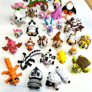 May include: A collection of colorful, handcrafted polymer clay animal figurines. The assortment includes a raccoon, flamingo, penguin, fox, and other creatures. Each figurine is uniquely designed with vibrant colors and detailed features.