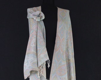 May include: A pastel-colored paisley scarf with a delicate fringe. The scarf is draped over a mannequin, showcasing its intricate design and soft color palette of pink, blue, and yellow. The scarf is made of a lightweight material.