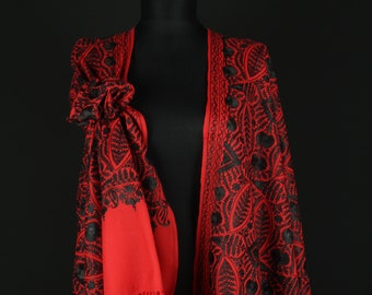 May include: A red shawl with black embroidery. The shawl has a fringe border and is draped over a mannequin.