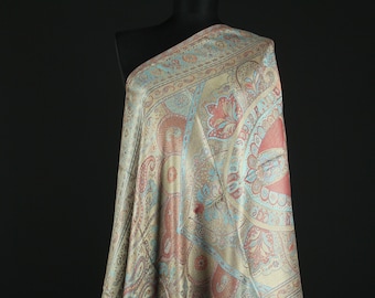 May include: A beige shawl with a paisley pattern in shades of blue, red, and gold. The shawl is draped over a mannequin and has fringe on the edges.