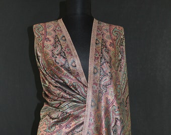 May include: A paisley patterned shawl with a black background and a beige border. The shawl is draped over a mannequin and has a fringe on the bottom.