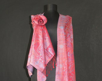 May include: A pink and blue paisley patterned scarf with fringe. The scarf is draped over a mannequin.