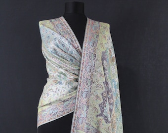May include: A white, green, and pink patterned shawl with a fringe border. The shawl is draped over a mannequin.