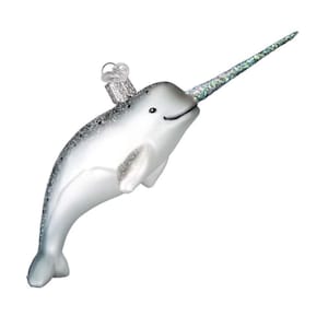 Może przedstawiać: Biała ozdoba świąteczna w kształcie narwala z błyszczącym rogiem i srebrnymi akcentami. Ozdoba ma uśmiechniętą twarz i małą pętelkę do zawieszenia. Ciało narwala jest gładkie i błyszczące.