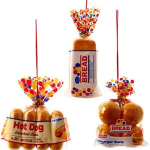 Puede incluir: Tres paquetes de productos de panadería, cada uno con un diseño de lunares coloridos y una cuerda para colgar. Los paquetes contienen bollos para hot dogs, bollos para hamburguesas y una hogaza de pan. Los paquetes están etiquetados como "Hot Dog Enriched Buns", "Classic Hamburger Buns" y "Bread".