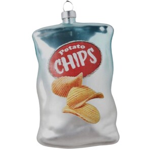 May include: A glass ornament shaped like a bag of potato chips. The bag is silver with a red circle that says "Potato Chips". There are three potato chips inside the bag.
