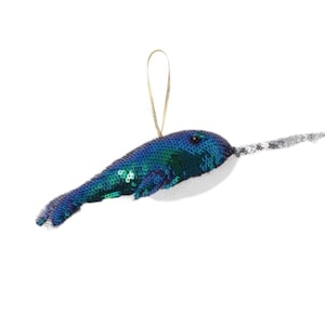 May include: A blue and green sequined narwhal ornament with a white belly and a gold string for hanging.