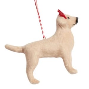 Peut inclure: Une décoration de chien en feutre beige avec un nœud rouge sur la tête. La décoration est suspendue à une ficelle rouge et blanche.