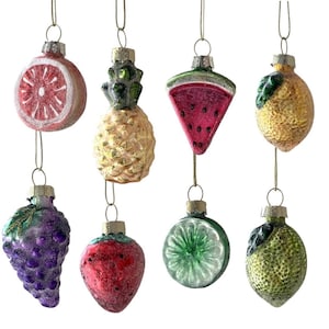 May include: A collection of eight glass Christmas ornaments shaped like various fruits. The ornaments include a grapefruit, pineapple, watermelon slice, lemon, grapes, strawberry, lime slice, and a lime. Each ornament has a silver cap and a gold string for hanging.