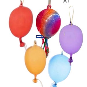 Puede incluir: Cinco adornos de vidrio con forma de globos en varios colores, incluyendo rojo, naranja, morado, azul y un globo iridiscente multicolor. Los adornos cuelgan de cuerdas. X1 está escrito en la esquina superior derecha de la imagen.