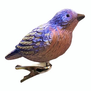 May include: A purple and brown glass bird ornament with gold glitter accents. The ornament has a metal clip on the bottom for hanging.