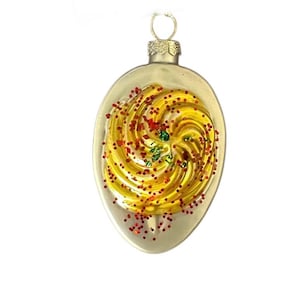 May include: A clear, teardrop-shaped Christmas ornament with a gold-colored swirl design. The swirl is decorated with red and green glitter. The ornament has a silver-colored metal cap and a loop for hanging.