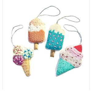 May include: Four beaded ornaments shaped like ice cream treats. Two are popsicles, one is orange and white, the other is blue and white. The other two are ice cream cones, one is pink and white, the other is green and white.