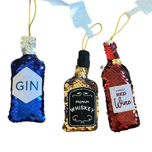 Op de afbeelding: Drie decoratieve flessieraden met paillettenstof. De flessen zijn blauw, goud en rood. De blauwe fles zegt "GIN", de gouden fles zegt "PREMIUM WHISKEY" en de rode fles zegt "FINEST RED WINE".