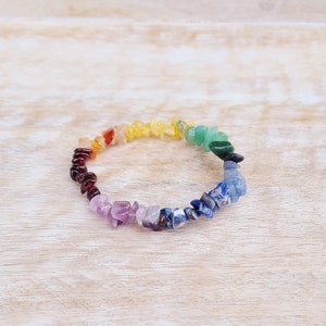 May include: A rainbow chakra bracelet made with natural gemstone chips. The bracelet features seven different colors of stones, including red, orange, yellow, green, blue, indigo, and violet.