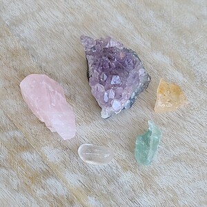 May include: A collection of five crystals: a large amethyst cluster, a rose quartz, a clear quartz, a green fluorite, and a yellow citrine.