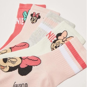 May include: A collection of five socks in various pastel shades, each adorned with a Minnie Mouse graphic. The socks display the word "NIE" and the Disney logo. The colour palette includes pink, white, and grey, with different Minnie Mouse designs.