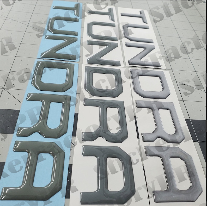 May include: Three sets of raised black plastic letters spelling out "TUNDRA" on white and blue backing paper.