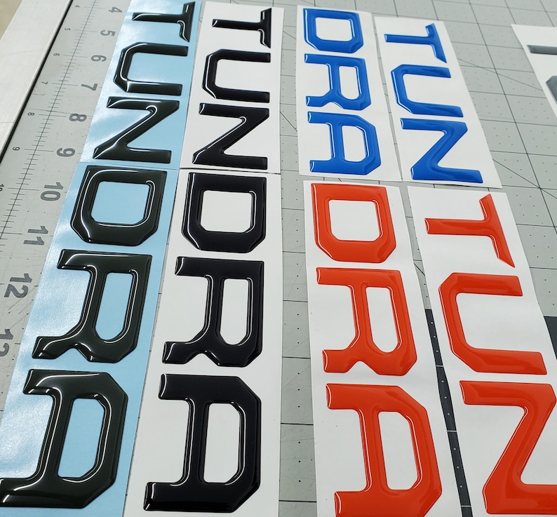 May include: Three sets of raised letters spelling out "Tundra" in black, blue, and red. The letters are on a white background.