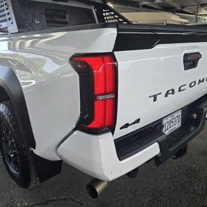 May include: A white Toyota Tacoma pickup truck featuring a black rear bumper, black fender flares, and a red taillight assembly with TRD branding. The tailgate displays the word TACOMA in black lettering, a 4x4 emblem, and a Puerto Rico license plate.