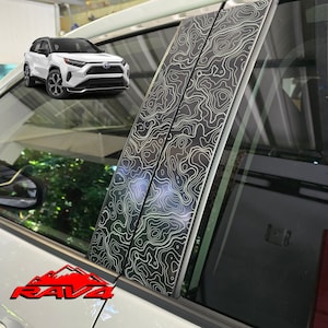 May include: A set of four black window pillar trim pieces with a white topographic map design. The trim pieces are designed to fit a Toyota RAV4.