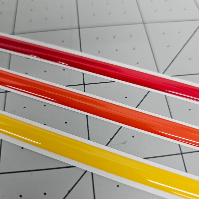 K&ouml;nnte beinhalten: Drei Streifen Klebeband in den Farben Rot, Orange und Gelb. Das Klebeband ist gl&auml;nzend und hat einen wei&szlig;en Rand.