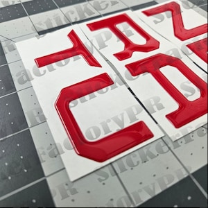 May include: Three red, 3D plastic letters, "C", "T", and "Z", on a white background. The letters are raised and have a glossy finish.