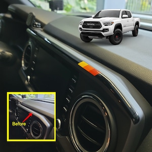 Peut inclure: Gros plan sur le tableau de bord d'une voiture avec une garniture noire et argentée. Le tableau de bord a une bouche d'aération et une rangée de boutons. Le mot "Avant" est écrit en rouge sur fond jaune dans le coin inférieur gauche de l'image.