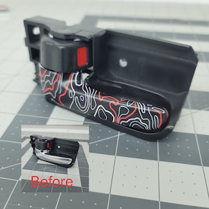 Puede incluir: Una manija de puerta de coche negra con un patrón abstracto rojo, blanco y negro. La manija se muestra junto a una manija similar con un acabado cromado. El texto "Antes" es visible debajo de la manija cromada.