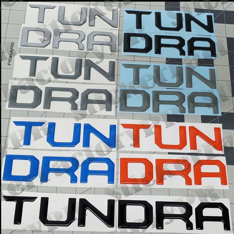 May include: A set of six black, grey, blue, and red vinyl decals with the words "Tundra", "Tun", and "Dra" in a 3D style.