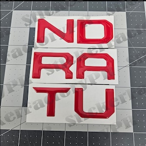 May include: Red vinyl letters spelling out "N-D-R-A-T-U" on a white background.