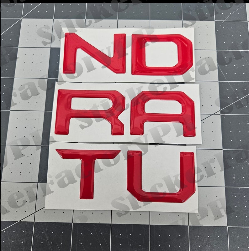May include: Red vinyl letters spelling out "N-D-R-A-T-U" on a white background.