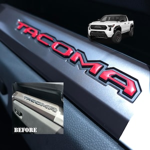 May include: A close-up of a silver truck bed with a red "TACOMA" emblem. The before image shows the same truck bed with a silver "TACOMA" emblem.