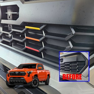K&ouml;nnte beinhalten: Nahaufnahme eines schwarzen LKW-K&uuml;hlergrills mit Wabenmuster. Der K&uuml;hlergrill hat drei rote, orange und gelbe Akzentstreifen. Der Text "VORHER" ist in der unteren rechten Ecke des Bildes sichtbar.