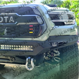K&ouml;nnte beinhalten: Die Front eines olivgr&uuml;nen Pick-ups mit einem schwarzen Wabengrill, drei horizontalen roten, orangen und gelben Lichtern, einer schwarzen Stahlsto&szlig;stange mit integrierter LED-Lichtleiste, einem silbernen Abschleppsch&auml;kel und einem Scheinwerfer.
