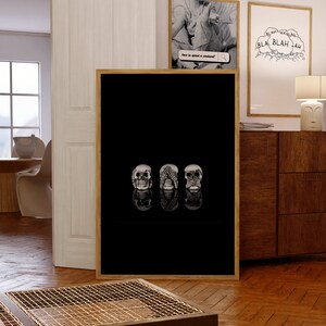 May include: A framed art print showing three skull sculptures, each in a different pose: one with eyes open, one with hands covering the eyes, and one with hands covering the mouth. The background is black.