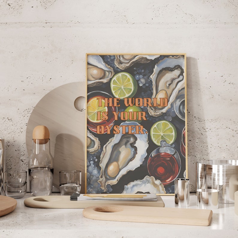 May include: A framed art print with the text "THE WORLD IS YOUR OYSTER" features oysters, lime slices, and red wine glasses on a dark background. The print is displayed on a white surface with wooden serving boards and glassware.