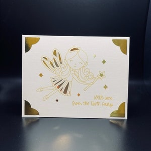 May include: A white card with gold corners and a gold outline of a fairy with a crown and wings. The card says "With love, from the tooth fairy".