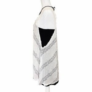 May include: White sleeveless tunic with a black geometric pattern. The tunic has a loose fit and a slightly longer length.
