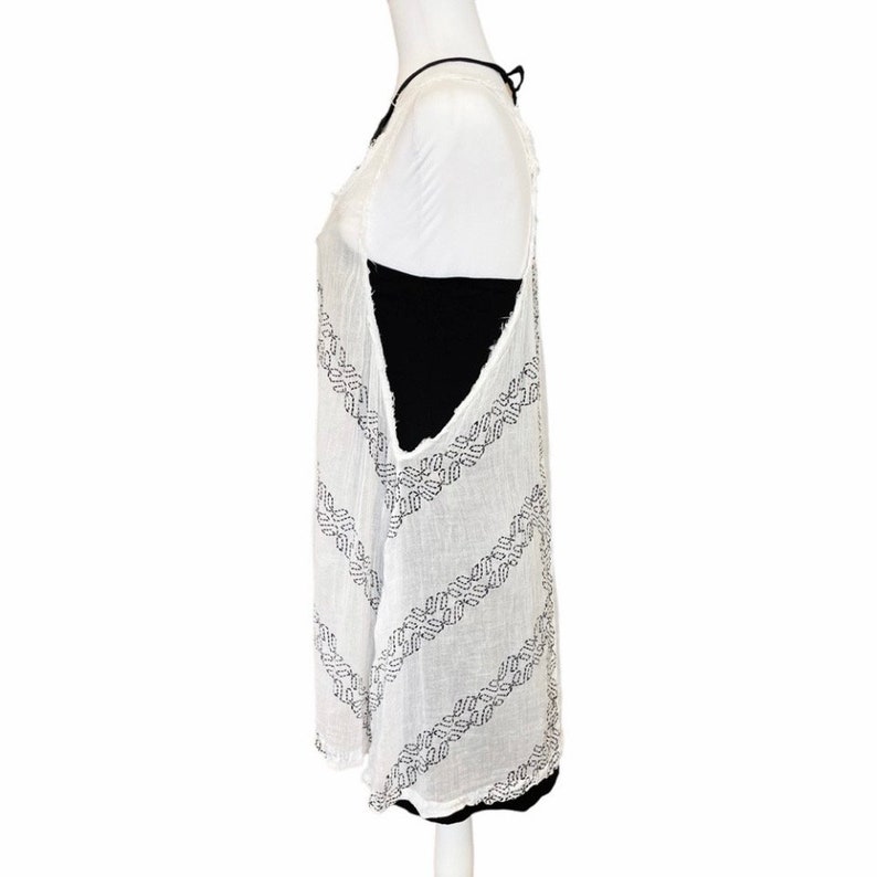 May include: White sleeveless tunic with a black geometric pattern. The tunic has a loose fit and a slightly longer length.