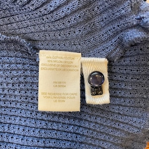 May include: A beige fabric tag with black text that reads "64% Cotton/Coton 36% Nylon/Nylon Exclusive of Decoration/Exclusivite de Decoration RN 66170 CA 32054 See Reverse for Care Voir L'inverse Pour Le Soin".