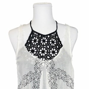 May include: White sleeveless top with black crochet detailing around the neckline. The top has a geometric pattern embroidered on the front.