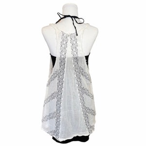 May include: White sleeveless top with black embroidered details. The top is sheer and has a loose, flowing fit.